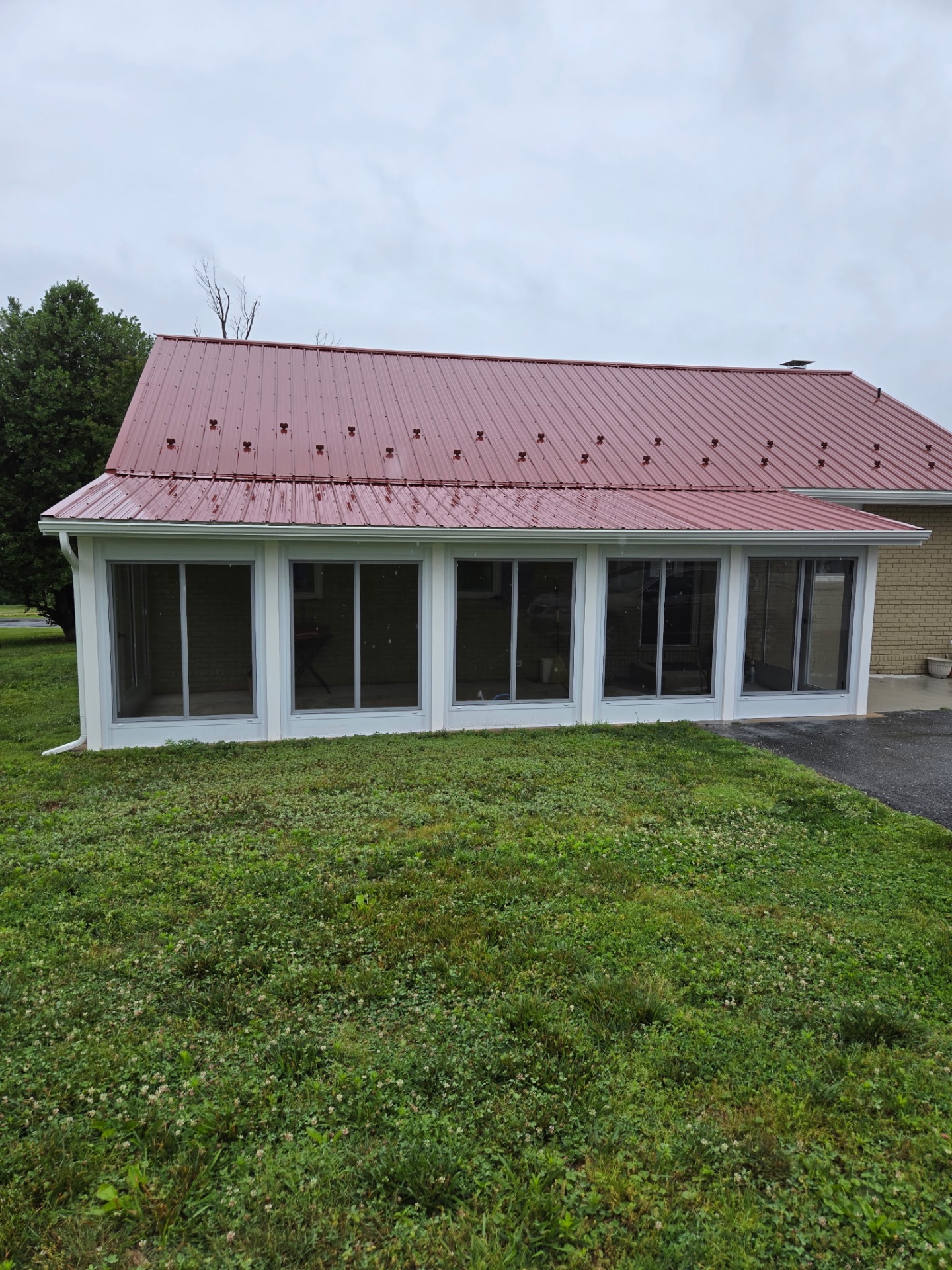 Sunspace WeatherMaster porch enclosure with five window bays on a Maryland brick home with red metal roof