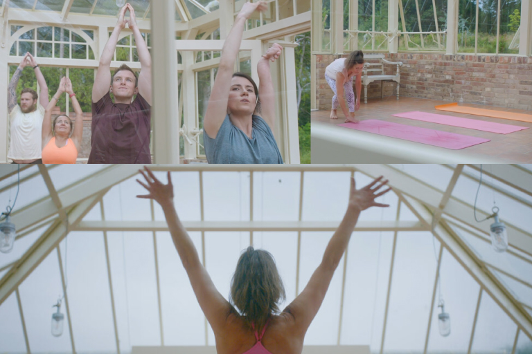 People stretching and practicing yoga on mats inside a bright glass greenhouse